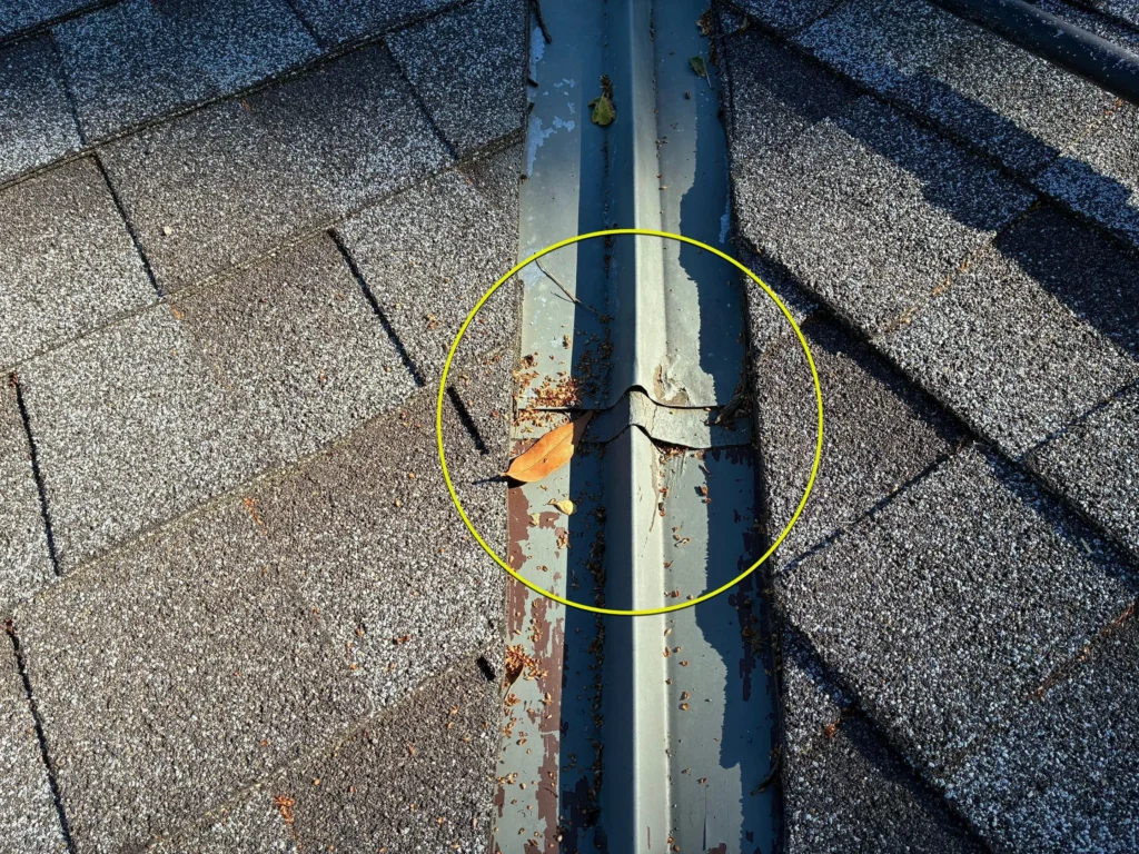 Damaged metal roof valley flashing seam with deteriorating coating and debris buildup.