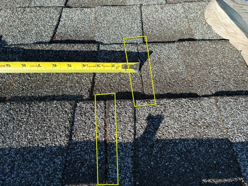Measuring tape highlighting improperly aligned asphalt shingle side laps during a roof inspection.