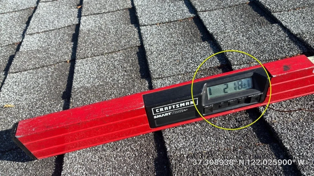 Digital level measuring the pitch of an asphalt shingle roof during a residential roofing inspection.